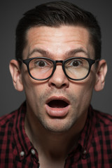 Wall Mural - Close-up portrait of surprised man in plaid shirt and wearing glasses on gray background