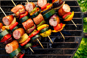 Wall Mural - Grilled skewers of meat, sausages and various vegetables on a grill plate, outdoors, top view. Grilled food, bbq