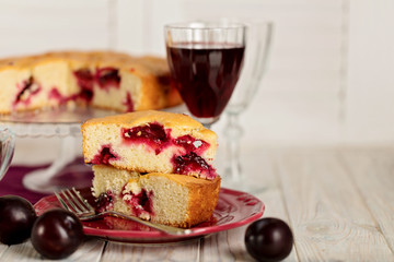 Homemade plum cake on a glass stand and red wine.