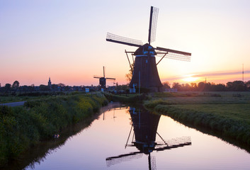 Sunset with traditional Dutch windmills reflected in the calm wa