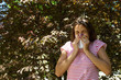 Young girl with allergy in autumn park. Sneezing girl blows her nose in a napkin