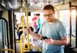 © dusanpetkovic1 - Young serious man is using his phone while standing in a bus and holding onto the yellow bar.