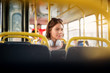© dusanpetkovic1 - A young pretty woman with headset hanging on her neck is using tablet while sitting on a bus seat.