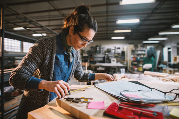 thoughtful middle-aged industrial female engineer with eyeglasses working with a tape measure in the