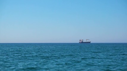 Poster - Calm sea with clear blue sky and cargo ship on the horizon