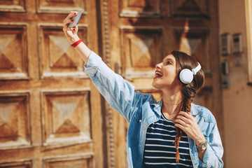 Wall Mural - Young woman listens to music via headphones and smartphone in the city