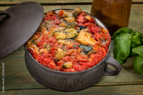 Fotografía Ratatouille in ceramic pot with Basil on wooden table