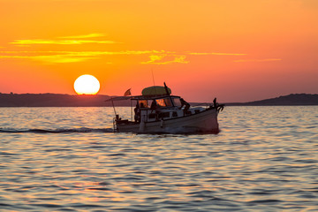 Sunset over sea with silhouette of small boat