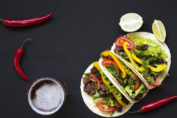 Tacos with beef and vegetables, beer and lime on a black background, top view. Mexican kitchen. Copy space. Flat lay.