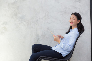 Wall Mural - Beautiful young asian woman touching tablet computer and smile sitting on cement background, freelancer female calling telephone, communication concept.