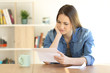 © Antonioguillem - Worried female reading a letter on a table at home