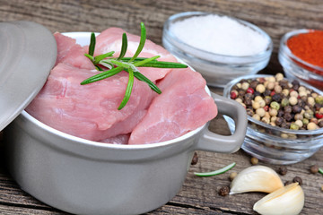 Wall Mural - Raw pork pieces in a pot and bowls with spices on old wooden table