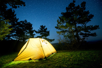 glowing camping tent in the night mountain forest under a starry sky