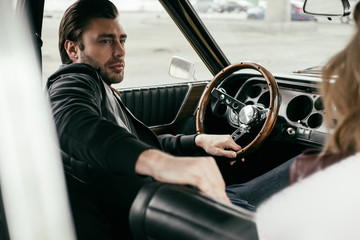 handsome stylish young man looking away while sitting in old-fashioned car