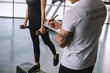 cropped image of male personal trainer writing in clipboard and young sportswoman doing step aerobics exercise with dumbbells at gym