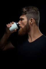 Indoor shot of serious confident young man drinking coffee Side view portrait of brutal bearded man holding expresso coffee cup on black background