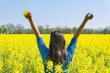 Happy woman arms up in yellow field of flowers