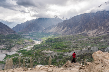 Wall Mural - photographer in red jacket taking landscape photograph on mountain peak cliff at hunza valley in pak