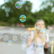 © Plutmaverick - Blurred background with shallow depth of field. The girl lets the soap bubbles in the park, has a fun weekend.