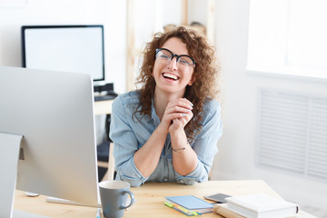 Beautiful and cheerful young female student wears glasses, smiling broadly at camera happy about the successful passing of an online exam