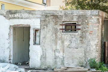 Small house near building with damaged door and walls with bullet holes used as improvised hidden prison with bars on the window in the war zone by terrorists in the Syria