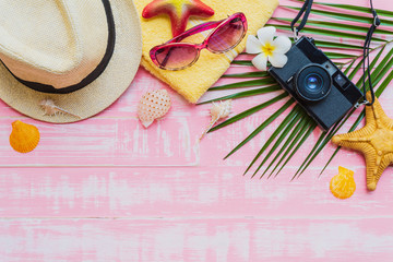 Beach accessories including sunglasses, sunscreen, hat beach, shell, green coconut palm leaves tree and retro camera on bright pink pastel wooden background for summer holiday and vacation concept.