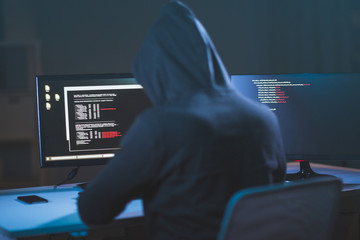 cybercrime, hacking and technology concept - male hacker in dark room writing code or using computer virus program for cyber attack