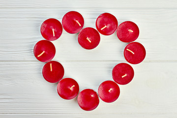 Shape of heart from red tea light candles. Red candles forming shape of heart on light wooden background, top view. Love and romance concept.