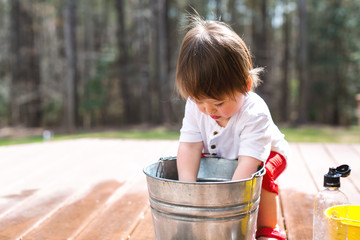 Happy toddler boy playing outside with buckets of water