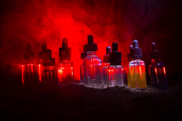 Vape concept. Smoke clouds and vape liquid bottles on dark background. Light effects. Useful as background or vape advertisement or vape background.