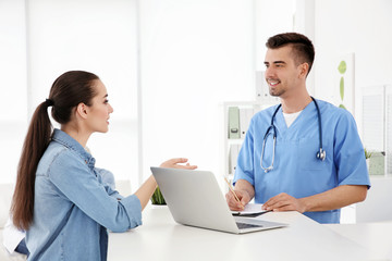 Canvas Print - Young male doctor working with client at reception desk in hospital