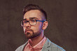 © Fxquadro - Close-up portrait of a confident stylish bearded man with hairstyle and glasses in a gray suit and pink shirt, posing in a studio.