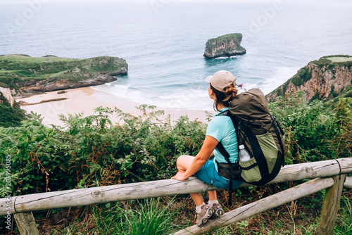 Fotografia  Traveler girl sits on wooden fence and looks on ocean beach
