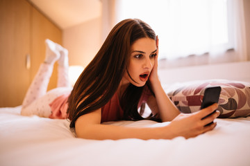 Young girl can't believe what she see on her phone while laying on her bed