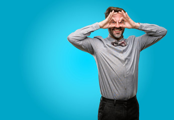 Canvas Print - Middle age man, with beard and bow tie looking at camera through fingers in ok gesture. Imitating binoculars