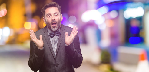 Canvas Print - Middle age man, with beard and bow tie happy and surprised cheering expressing wow gesture at night club