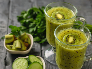 Two glasses of freshly made kiwi and cucumber smoothies on a dark rustic table.