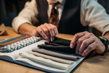 cropped shot of tailor working with cloth samples at sewing workshop in late evening