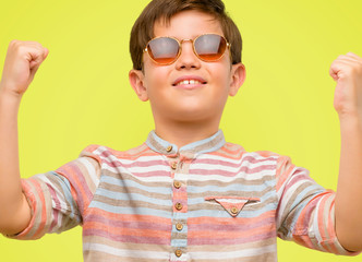 Handsome toddler child with green eyes happy and excited celebrating victory expressing big success, power, energy and positive emotions. Celebrates new job joyful over yellow background