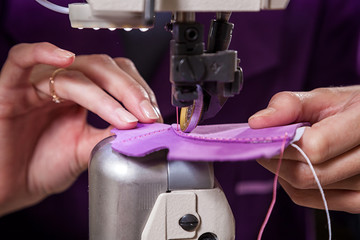 Close-up of a young woman working as a seamstress in a purple unifrome sews genuine leather children's shoes on a sewing machine