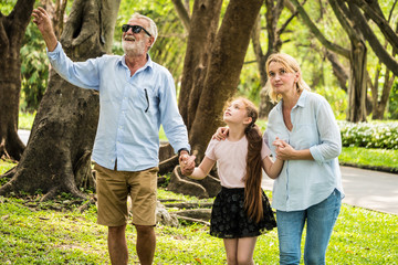 Wall Mural - Happy family having fun together in the garden. Father, mother and daughter holding hands and walking in a park. Lifestyle concept