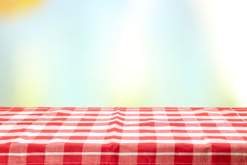 An empty table with a red checkered tablecloth and an pastel colorful natural background on a  sunny day. For your food and product display montage.