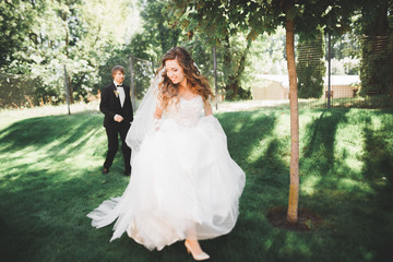 Stylish couple of happy newlyweds walking in the park on their wedding day with bouquet