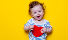 Little Baby With Heart Shape Toy On Yellow Background