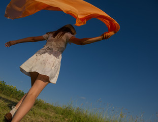 Wall Mural - BEAUTIFUL BLONDE GIRL LAUGHS AND DANCES OUTDOORS WITH AN ORANGE SCARF IN HER HANDS