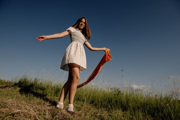 Wall Mural - BEAUTIFUL BLONDE GIRL LAUGHS AND DANCES OUTDOORS WITH AN ORANGE SCARF IN HER HANDS