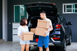 © twinsterphoto - Mature happy Asian married couple carrying cardboard boxes from car trunk at new home