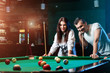 © Aliaksandr Marko - A guy and a beautiful girl are playing billiards, a guy is teaching a girl to play billiards. Dark background. Pleasant pastime, family rest, entertainment, holiday.