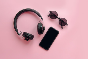 Wall Mural - stylish black sunglasses,smartphone and headphones on pink background, flat lay. modern hipster image. black items on pink paper. instagram blogging. space for text. summer vacation