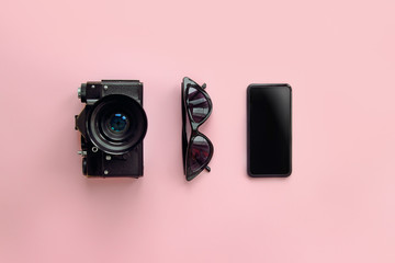 Wall Mural - summer travel concept. stylish black sunglasses,smartphone and photo camera on pink background, flat lay. modern hipster image. instagram blogging. space for text. summer vacation